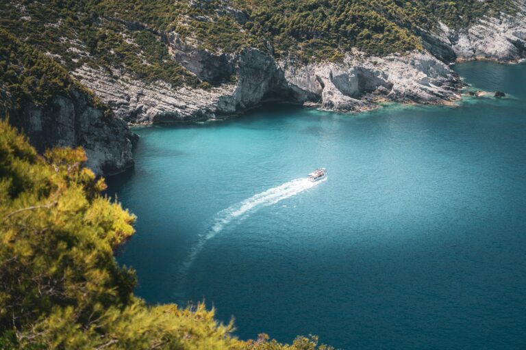 A small boat cruising through turquoise waters along a rocky coastline in Zakynthos, Greece