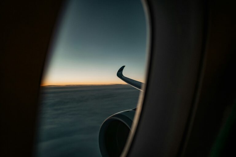 An airplane wing viewed through a window against clouds and a sunset sky
