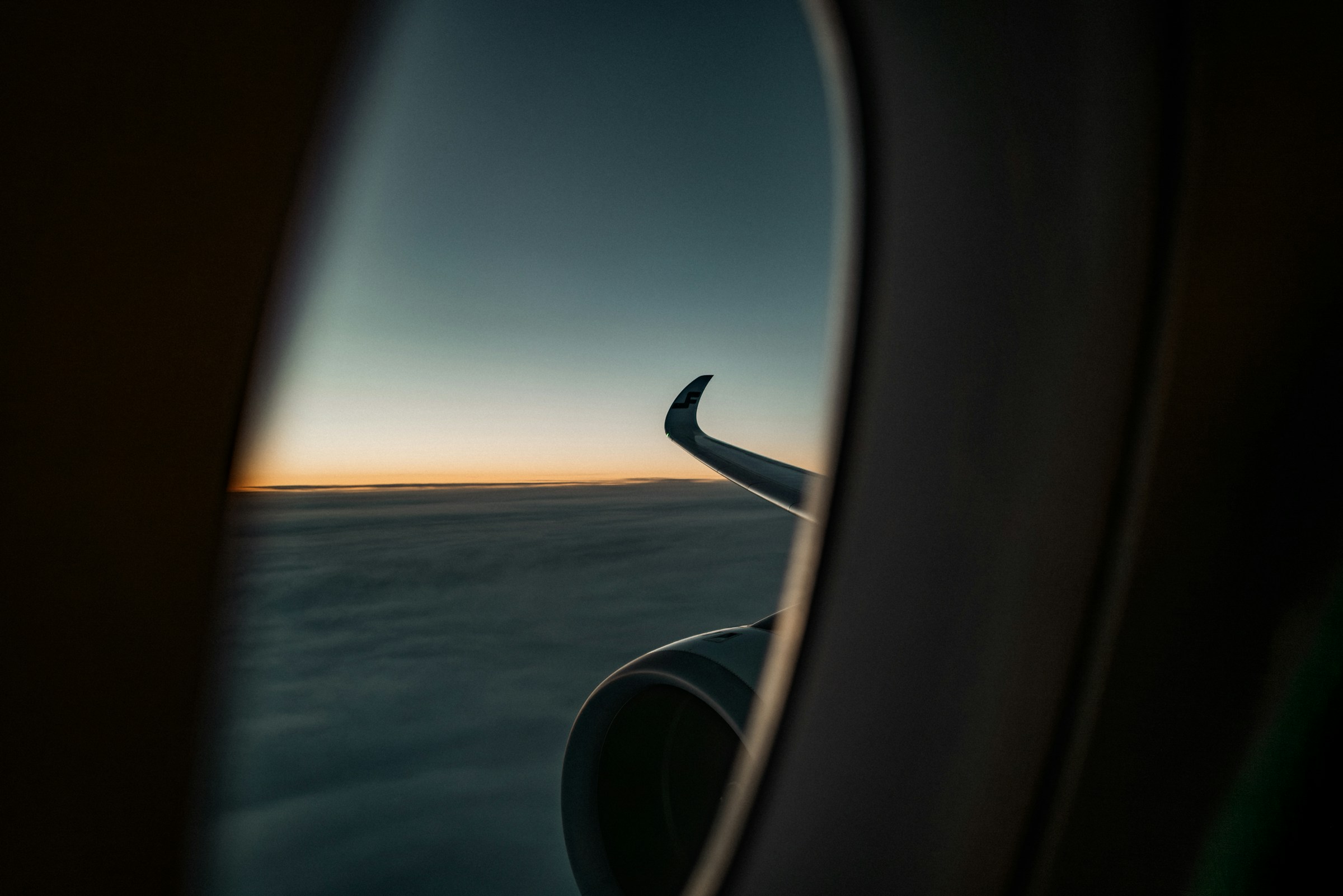 An airplane wing viewed through a window against clouds and a sunset sky