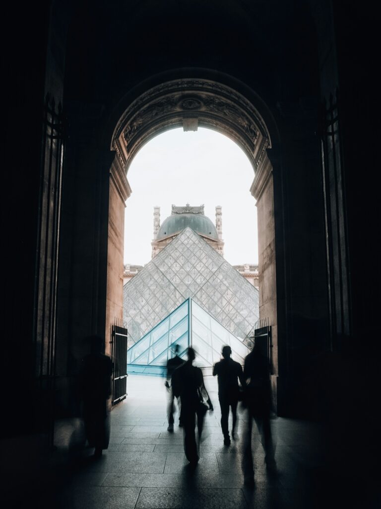 Visitors silhouetted against the glass Louvre Pyramid at golden hour in Paris