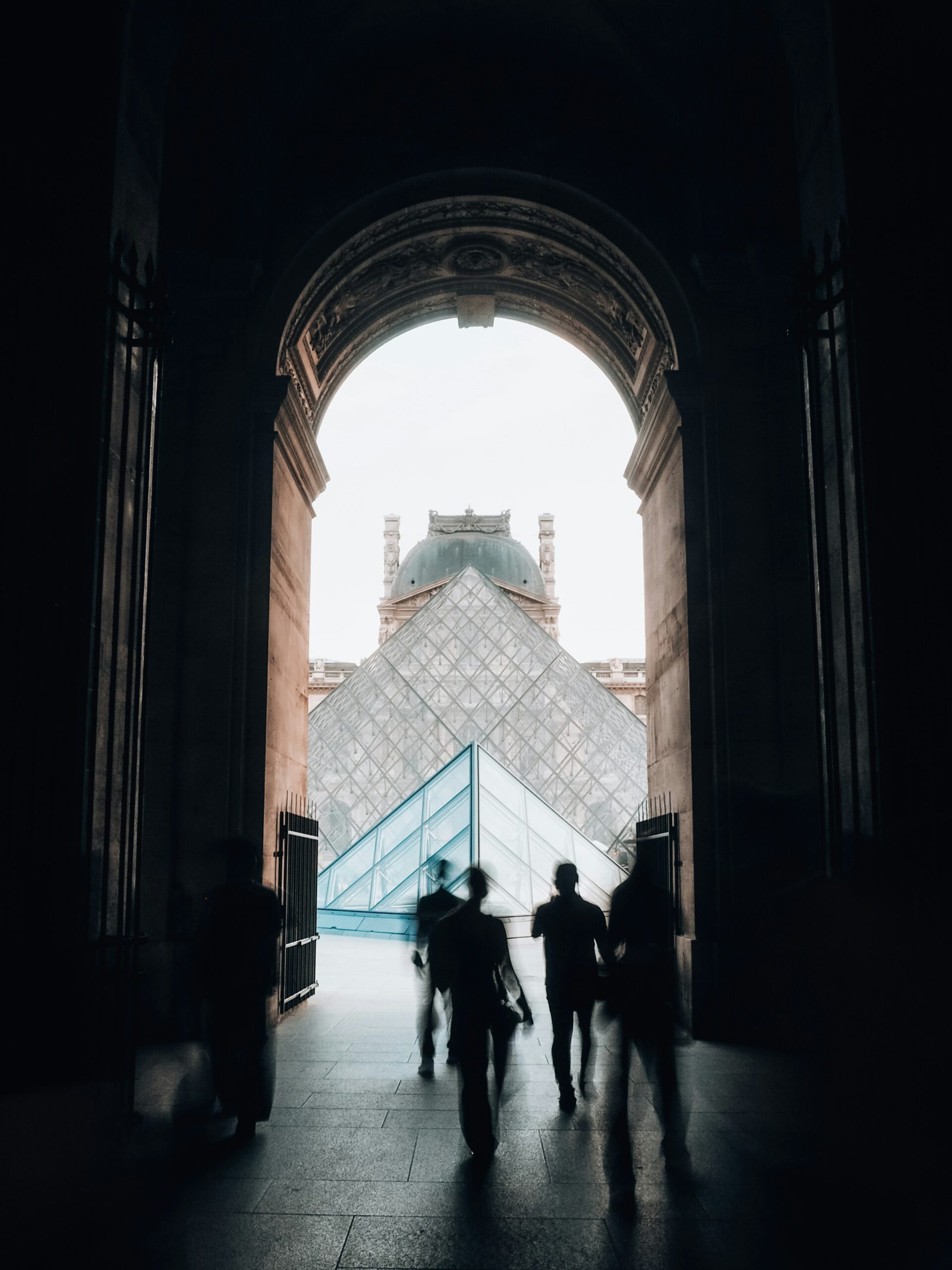 Visitors silhouetted against the glass Louvre Pyramid at golden hour in Paris