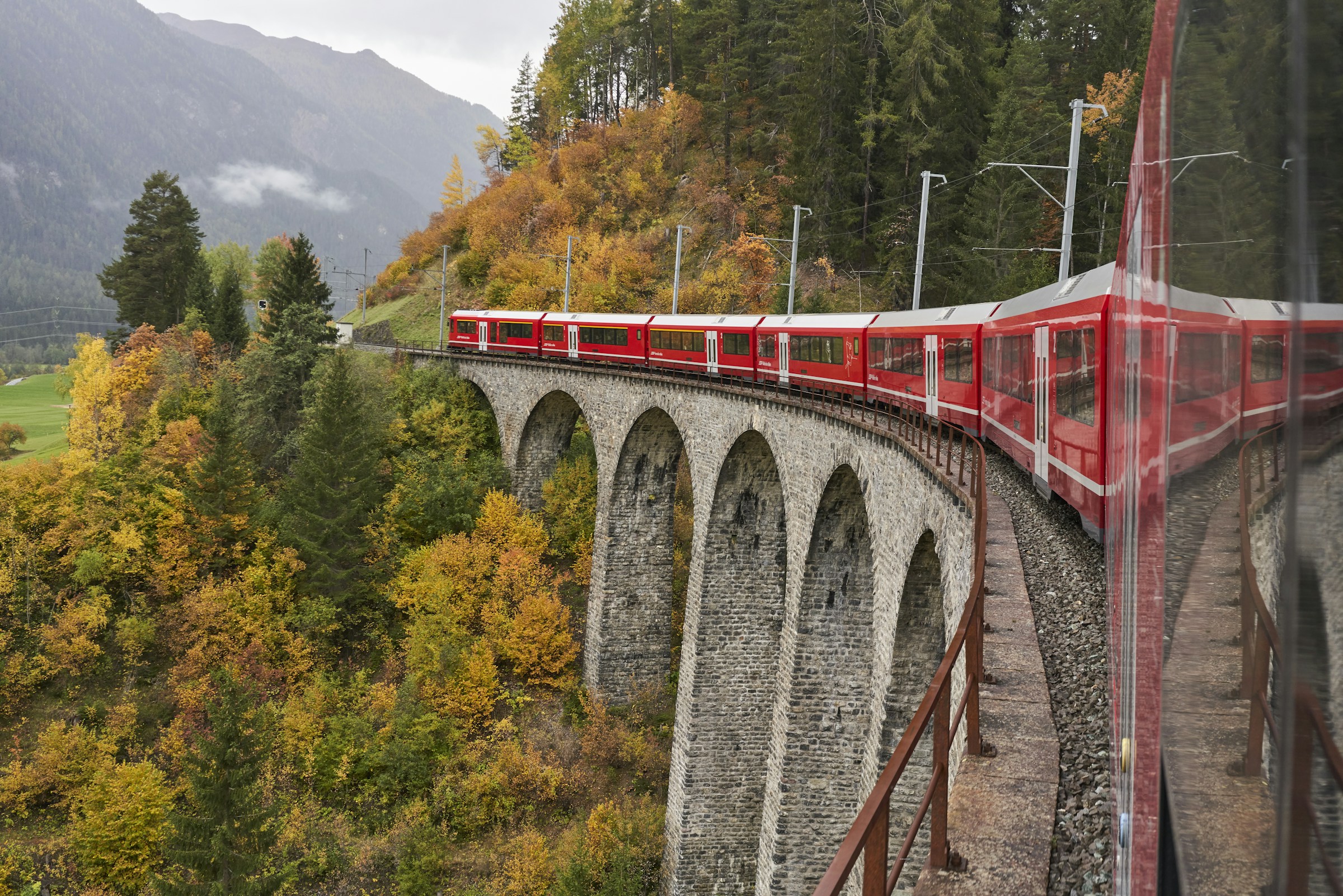 A red Rhaetian Railway train crossing a stone viaduct in the Swiss Alps near Bergun