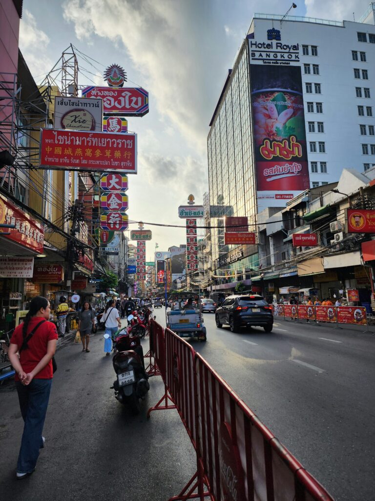 A busy Bangkok street in the Yaowarat Chinatown district with motorcycles, shop signs, and pedestrians