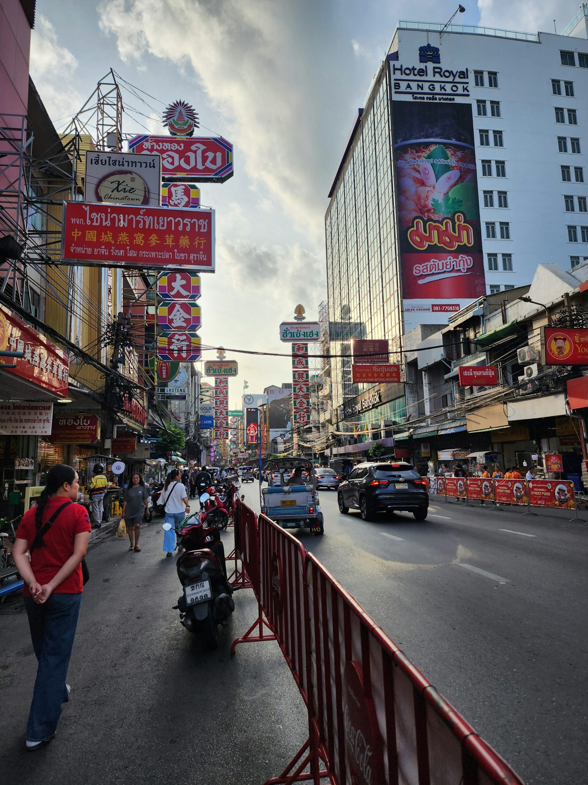 A busy Bangkok street in the Yaowarat Chinatown district with motorcycles, shop signs, and pedestrians
